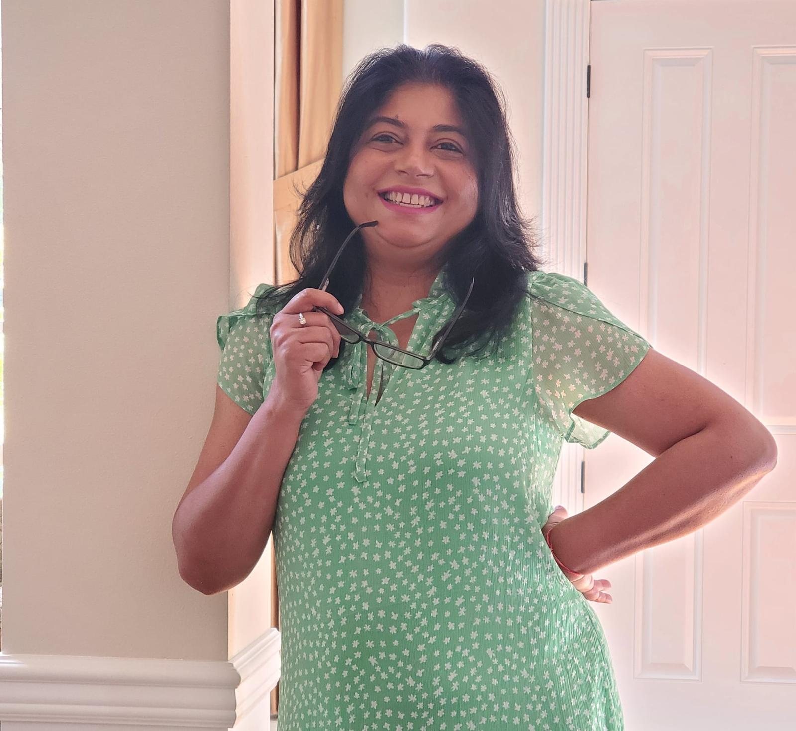 Sanchita smiling in a green dress and holding her glasses